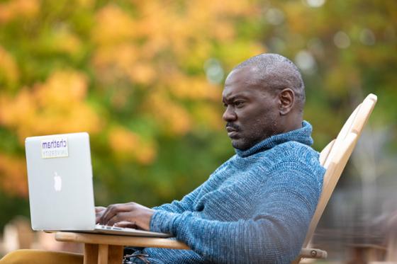 Photo of a Chatham University male student working on his laptop outside, 以秋叶为背景.