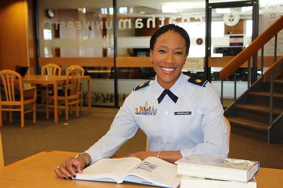 Photo of a woman in military uniform sitting at a library desk, 微笑, 在她面前打开一本书