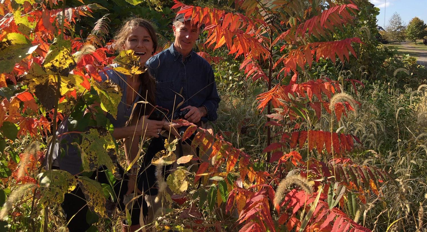 Photo of a man and woman smiling while walking through Chatham University's arboretum together surrounded by colorful leaves.