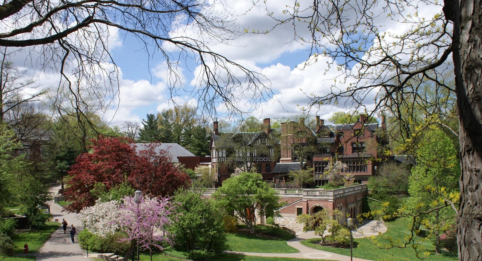 Redbrick academic buildings on Chatham University's Shadyside campus are framed by colorful budding trees and green grass. 